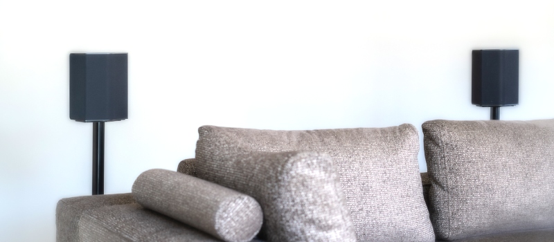 Graues Sofa mit zwei schwarzen Lautsprechern auf schwarzen Lautsprecherständern dahinter
