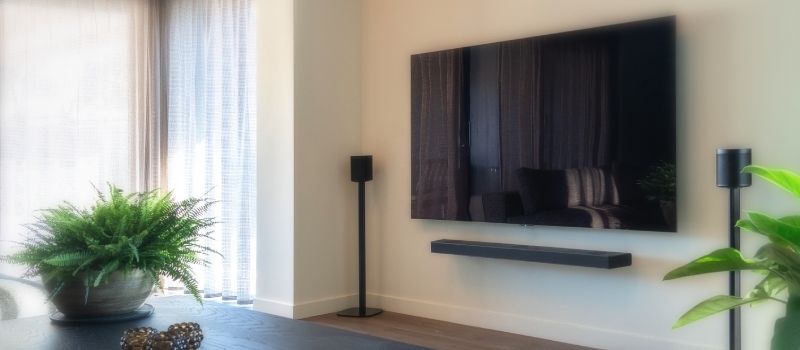 Schritt für Schritt die richtige Sehhöhe bestimmen Fernseher mit Lautsprechern links und rechts vor einer weißen Wand in einem hellen Wohnzimmer.