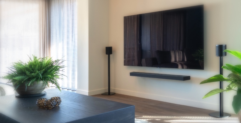 Ein Fernseher an der Wand mit zwei Lautsprechern daneben auf Lautsprecherständern im Wohnzimmer