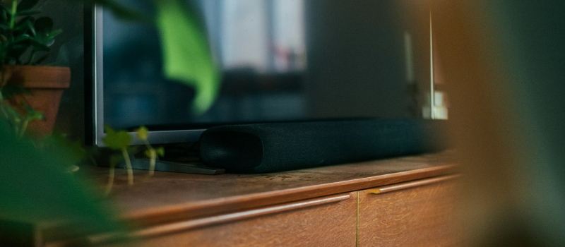 Bring deine Filmabende mit einer Soundbar auf ein neues Level Nahaufnahme einer eleganten, dunklen Soundbar auf einem Holzmöbelstück.