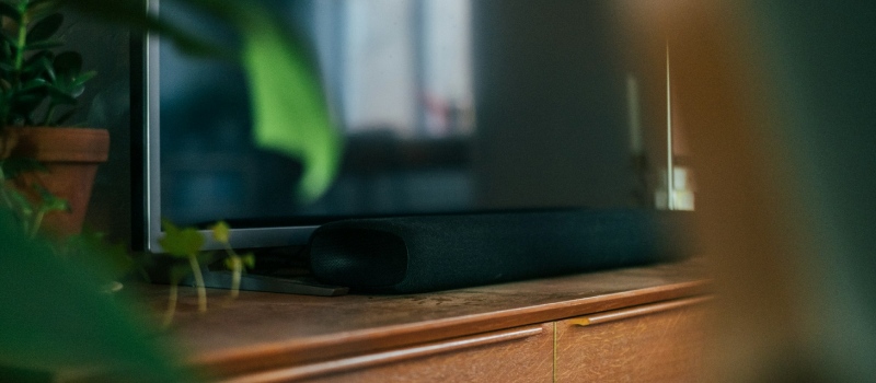 Was sollten Sie beim Kauf einer Soundbar beachten? Nahaufnahme eines Fernsehers, umgeben von Pflanzen, auf einem TV-Möbel, unter dem sich eine Soundbar befindet.